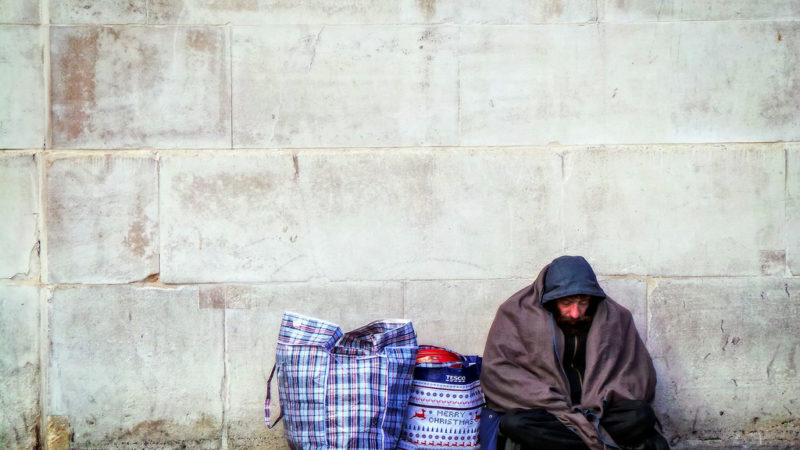 A homeless person sheltering under a concrete wall