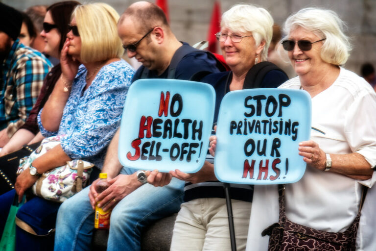 Campaigners holding signs reading "No health selloff" and "Stop privatising our NHS"
