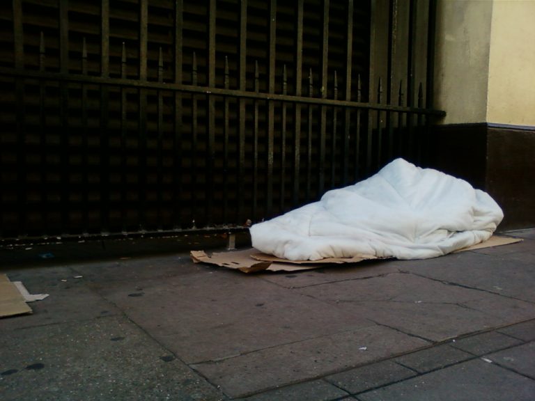 A photo of a blanket laying on cardboard boxes on a street