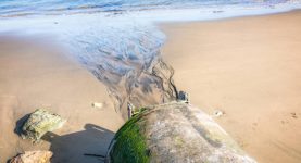 Fluid from a large concrete pipe on the beach creating flow patterns in the sand on a path to the sea.