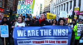 A photo of a march coinciding with RCN strikes. Demonstrators are carrying a banner reading "We are the NHS!"