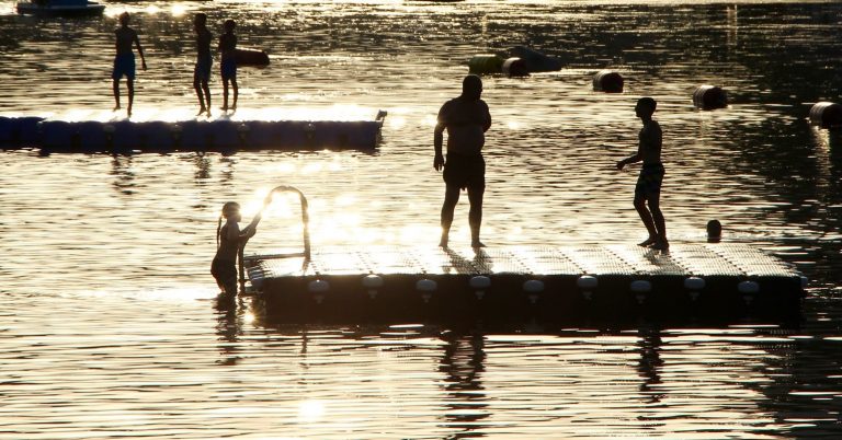 A photo of people standing around and swimming in a lake