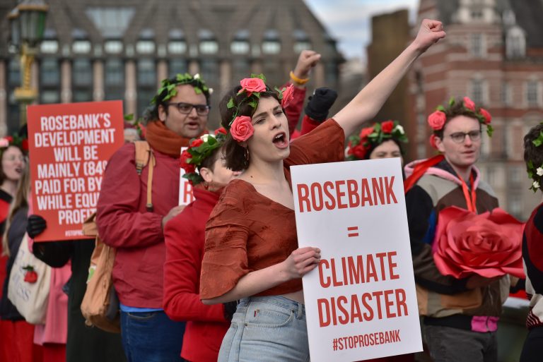 Campaigners dressed in red on Westminster Bridge with a placard reading 'Rosebank=Climate Disaster"